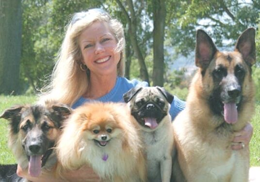 A woman standing with four dogs in front of trees.